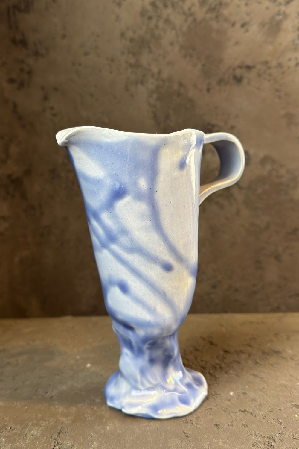 Close-up of the handle of a blue ceramic carafe, showcasing its glossy finish and fluid design.