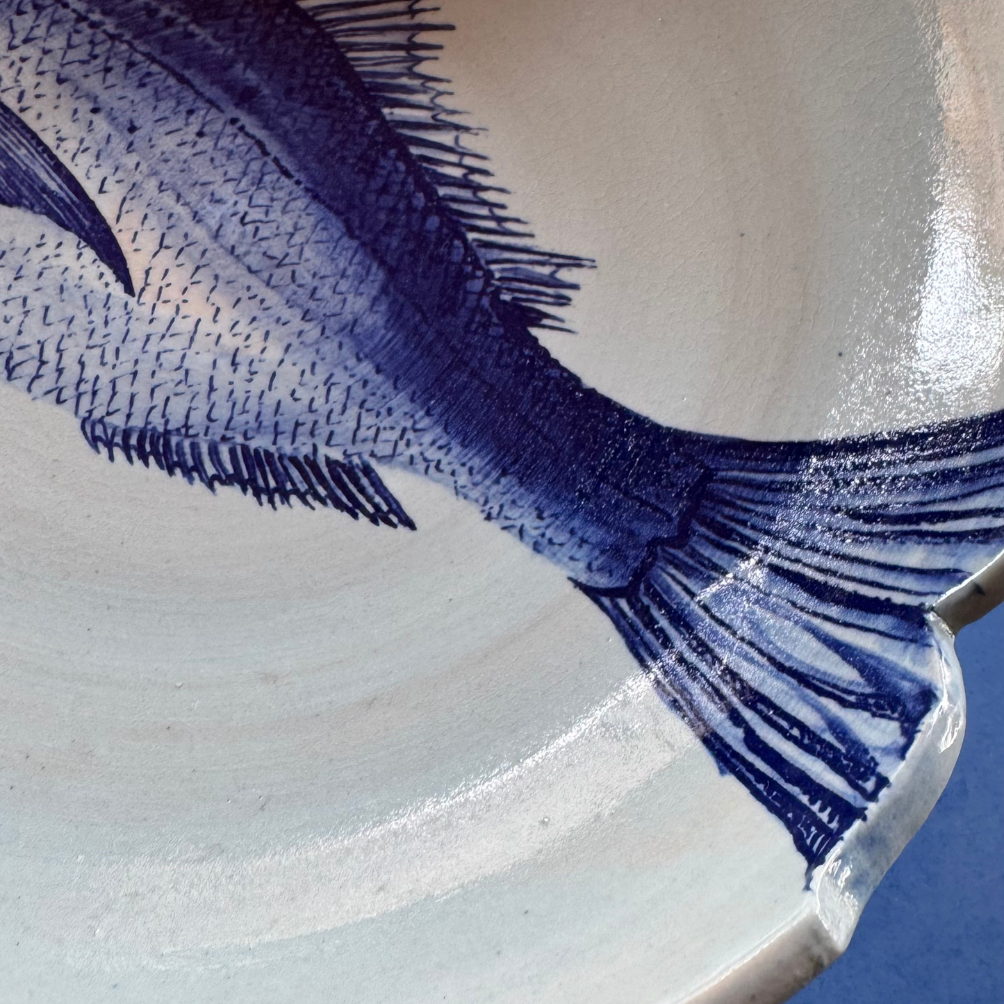 Close-up of the deep-blue dorade fish tail, showcasing the artisan brushwork and natural glaze texture on the light ceramic surface.