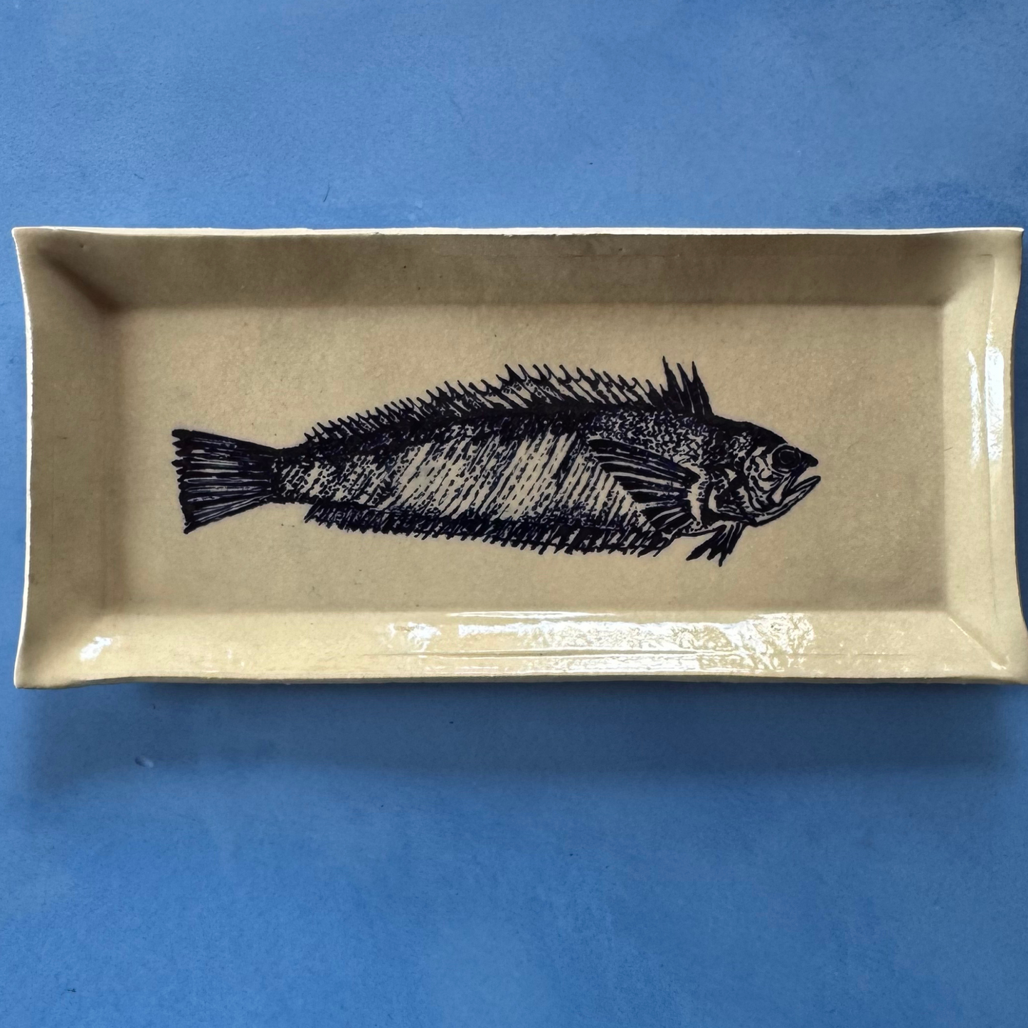 Schuine weergave van de serveerschaal, die de glanzende diepe blauwe afwerking en de zwarte visillustratie toont.