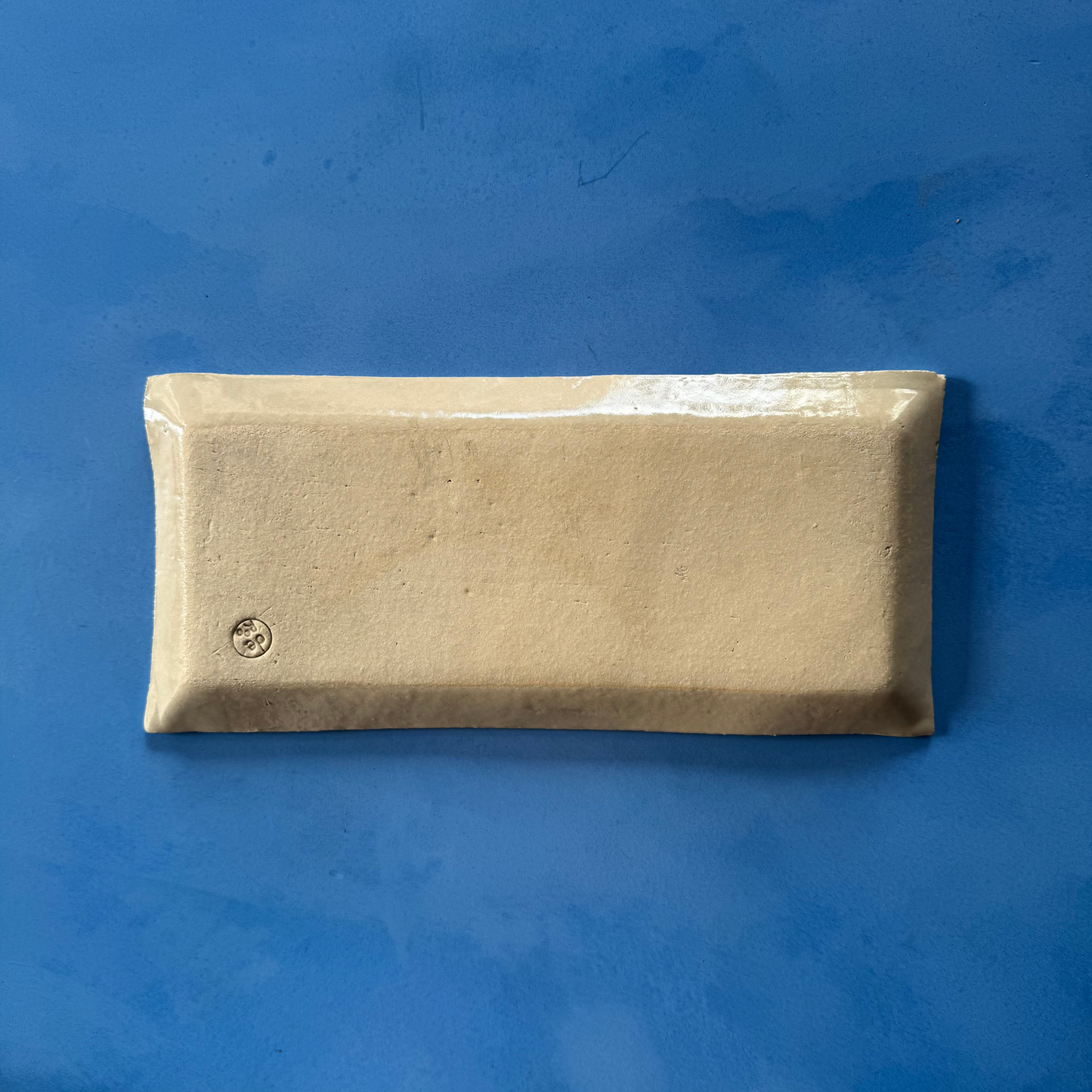 Achteraanzicht van de serveerschaal, met onbewerkt keramiek en het discrete makerstempel van QM Ceramics.
