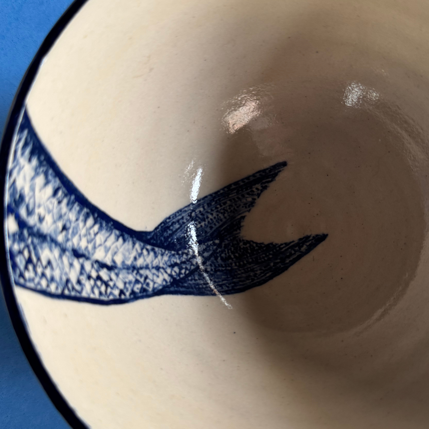 Zijaanzicht van de keramische kom met de diepblauwe rand en subtiel aangebrachte staartillustratie.