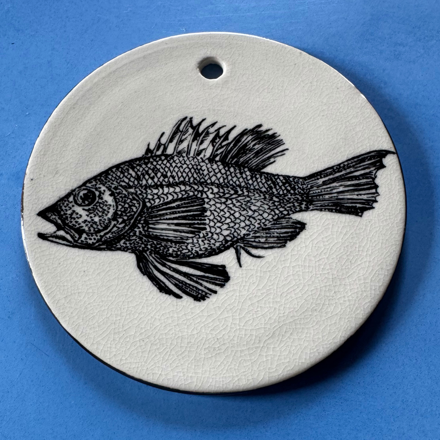 Bovenaanzicht van de handgeschilderde zwarte dorade-vis op het 14 cm keramische wandbord met craquelé glazuur.