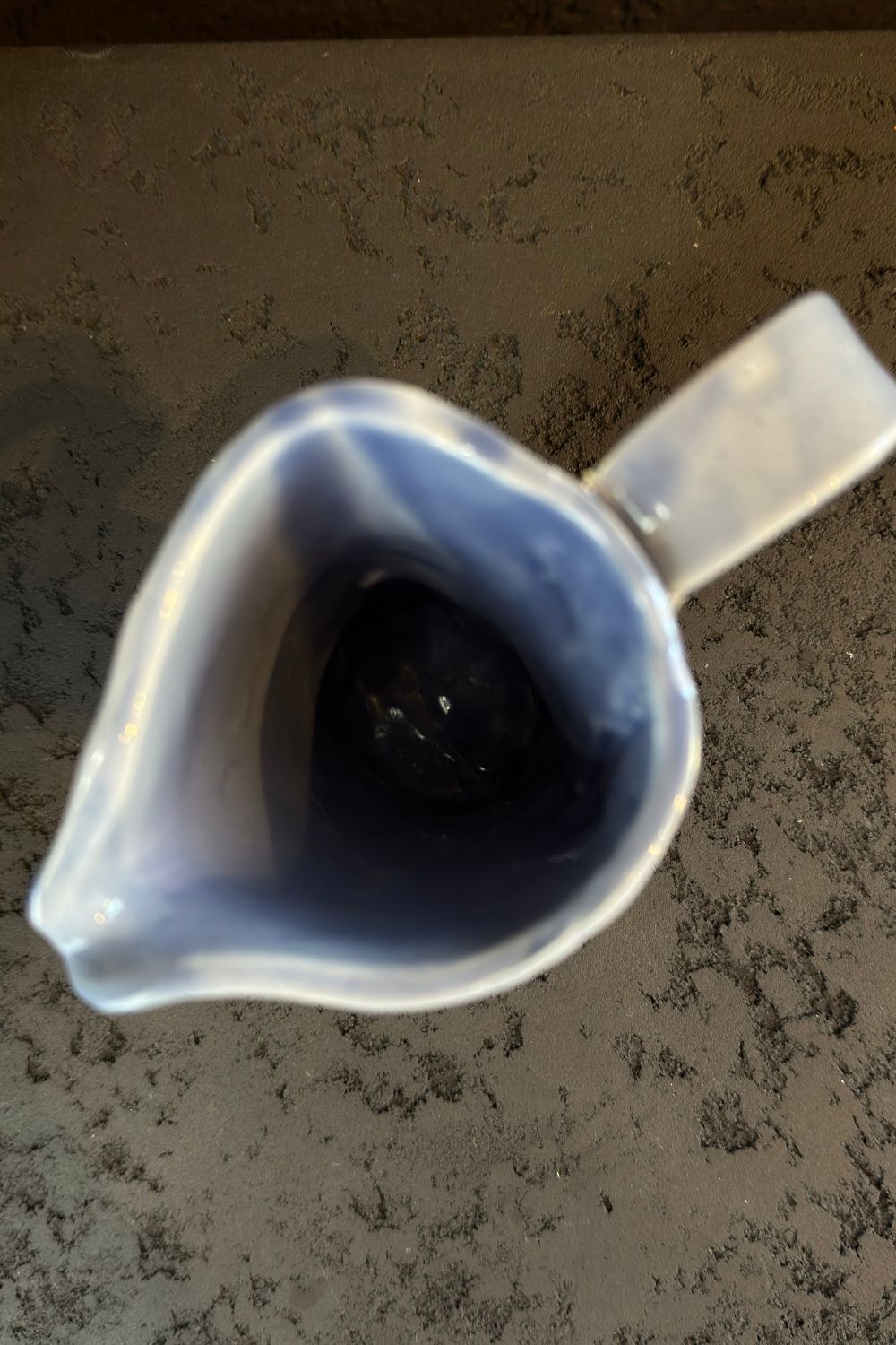 Close-up image of a blue ceramic carafe being held, showing the intricate glaze patterns.