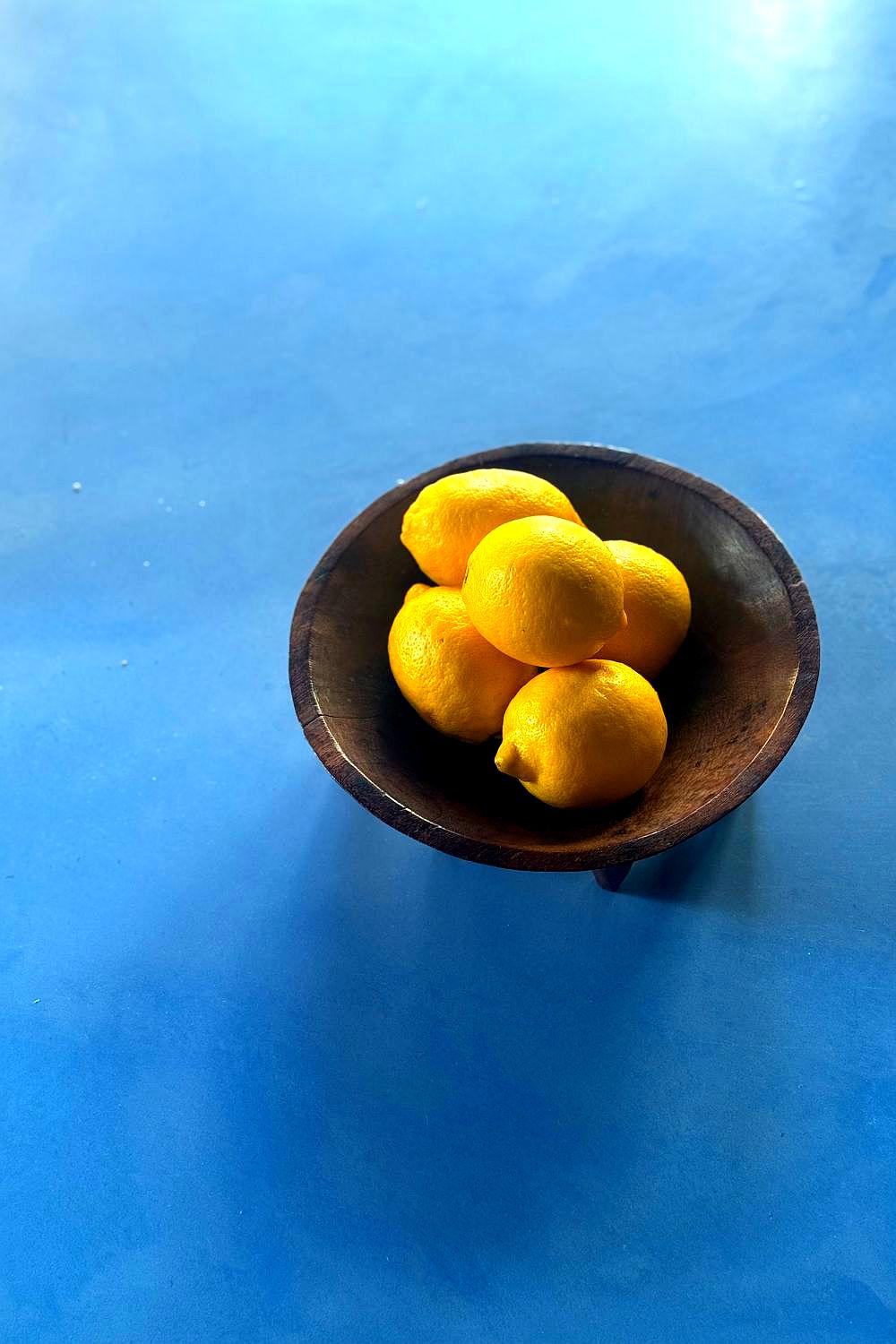 Fijian wooden tanoa kava bowl standing on six legs, filled with fresh lemons
