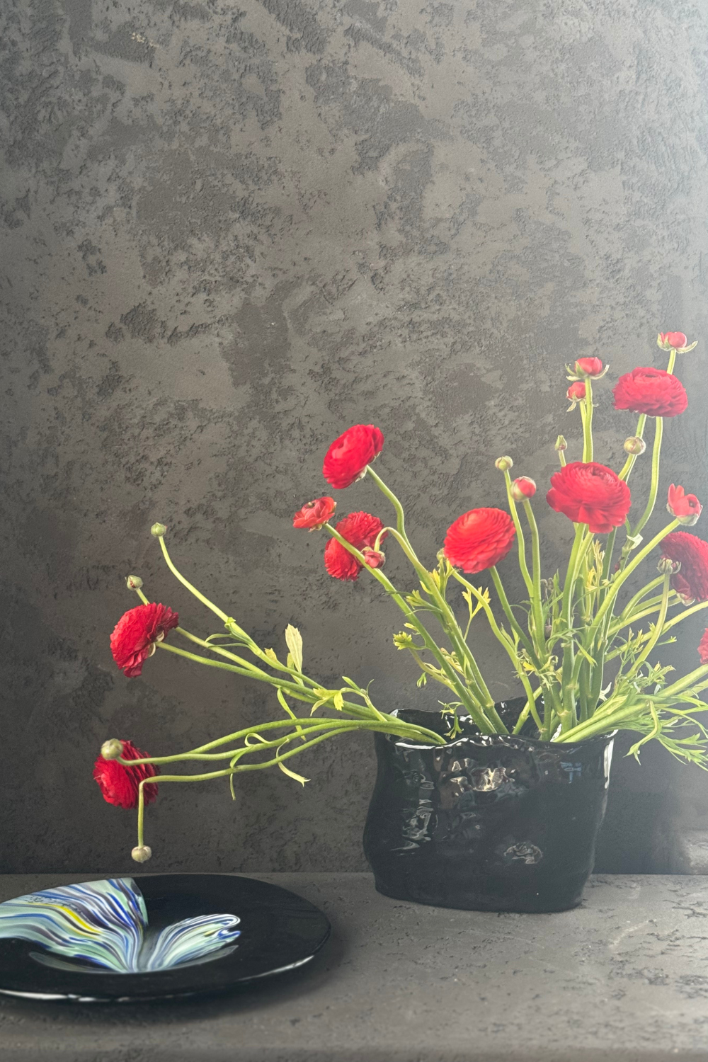 Black ceramic vase with red flowers, handcrafted by D E L F I N ceramics, displayed against a white background.