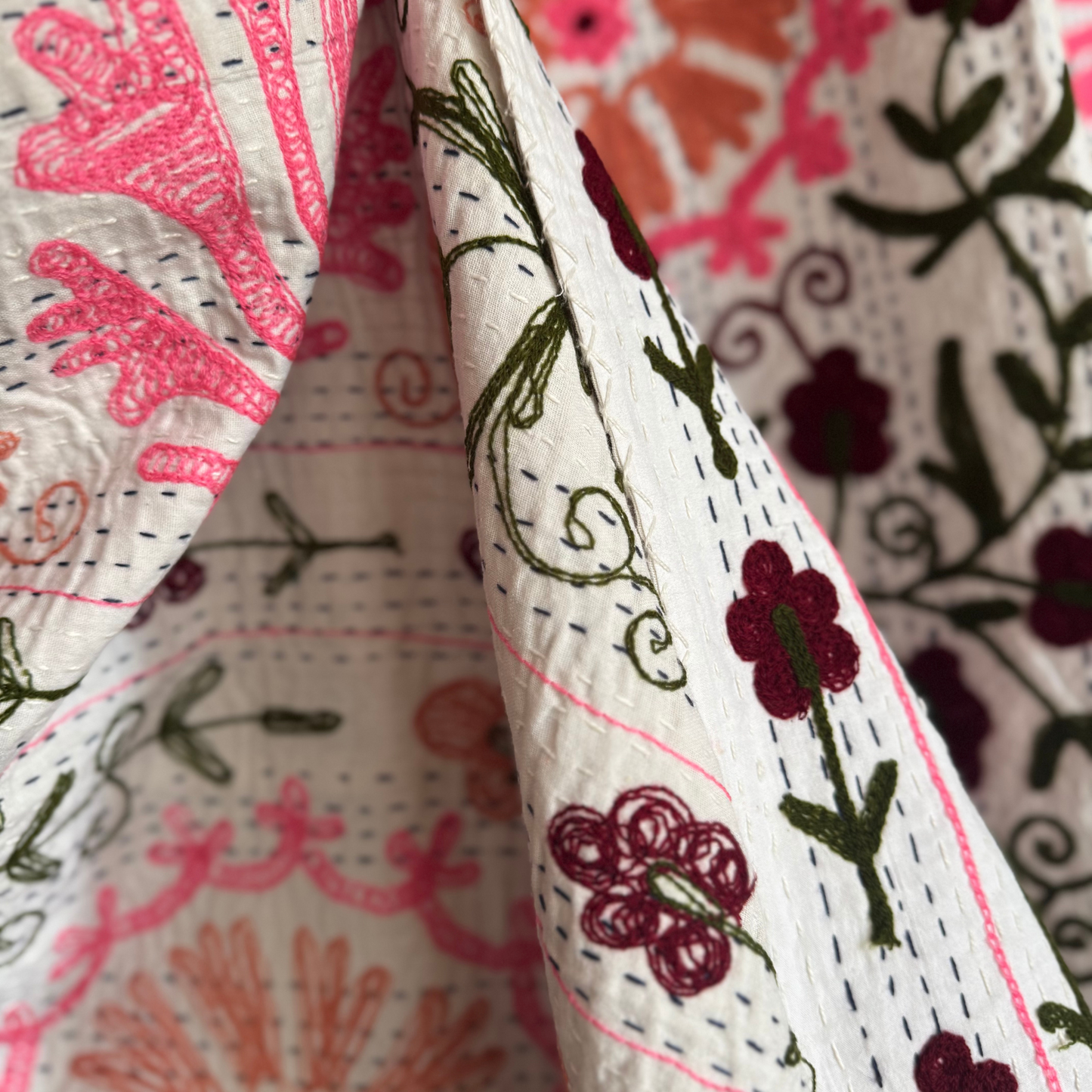 Close-up of small bordeaux flower clusters and green leaves embroidered on white ground