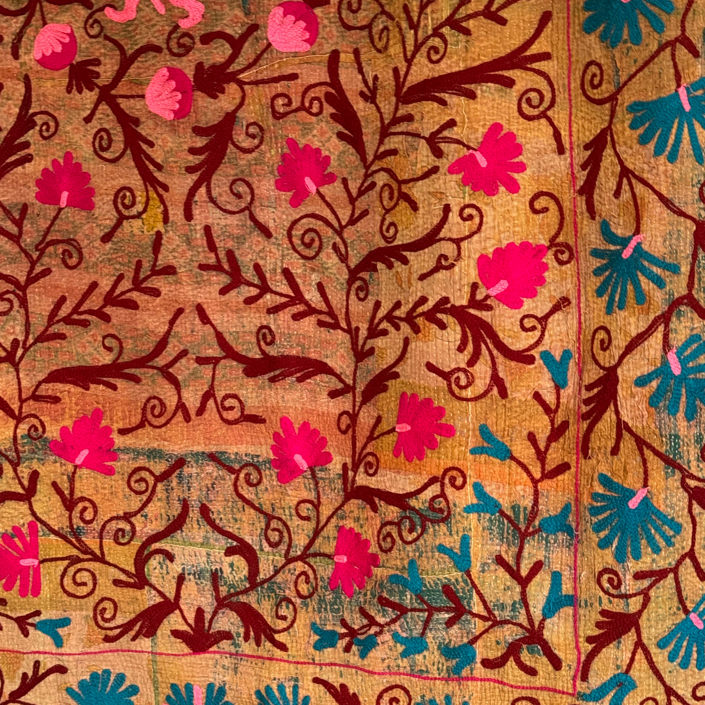 Zoomed embroidery detail of maroon vines and fuchsia flowers on a rich, multi-tonal cotton background