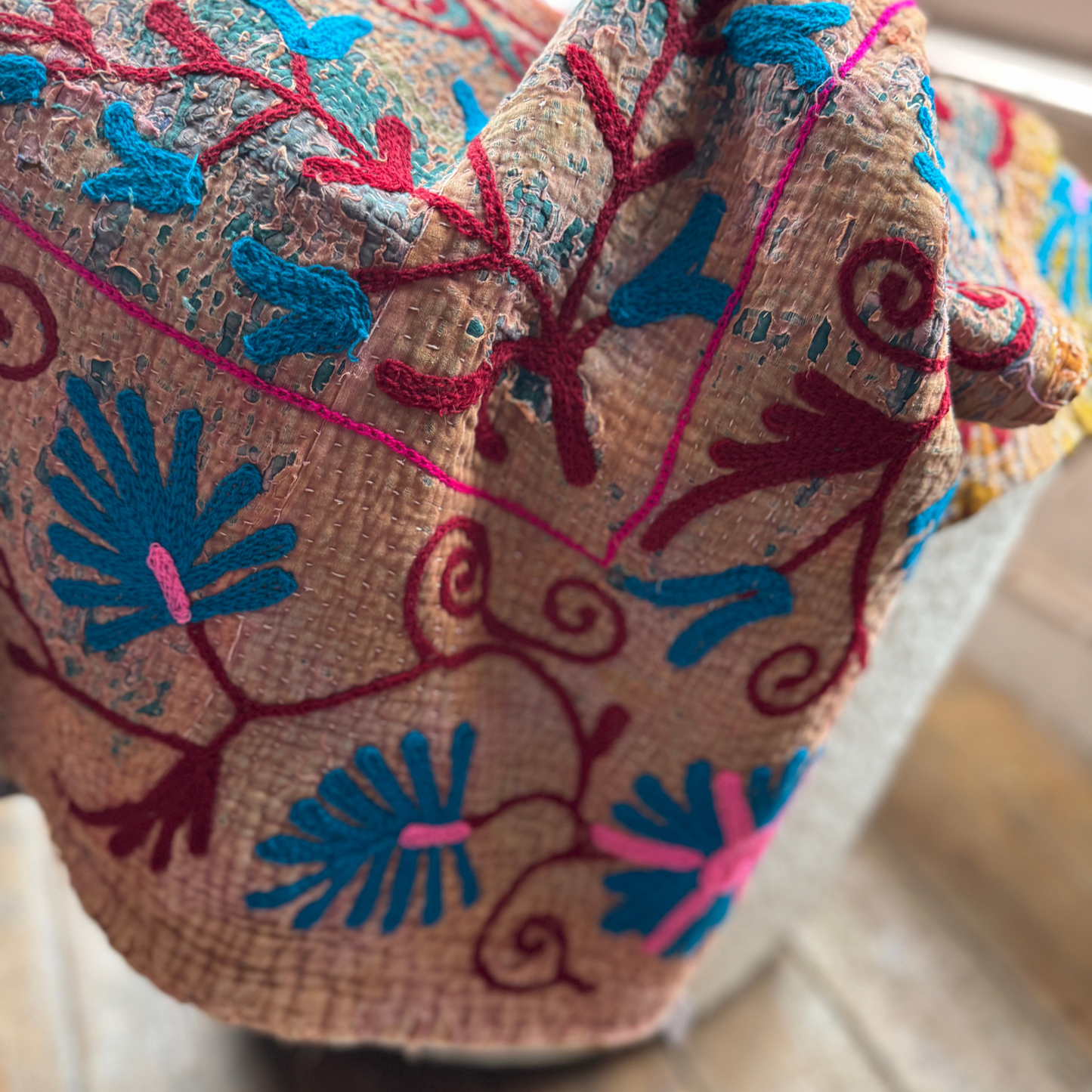 Detail of kantha front showing textured floral embroidery in sky blue, fuchsia and maroon on tan base