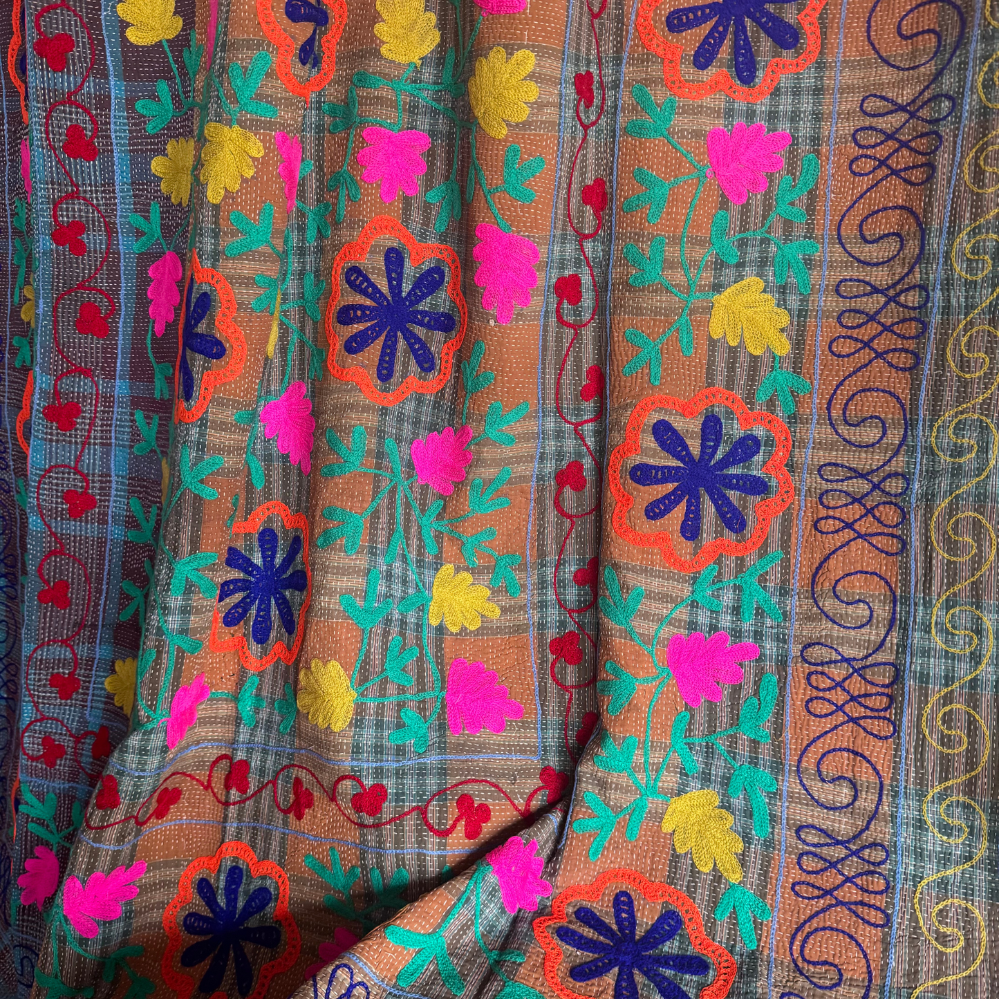 Close-up of rust-orange floral medallions and olive-green vine embroidery on cotton Kantha throw