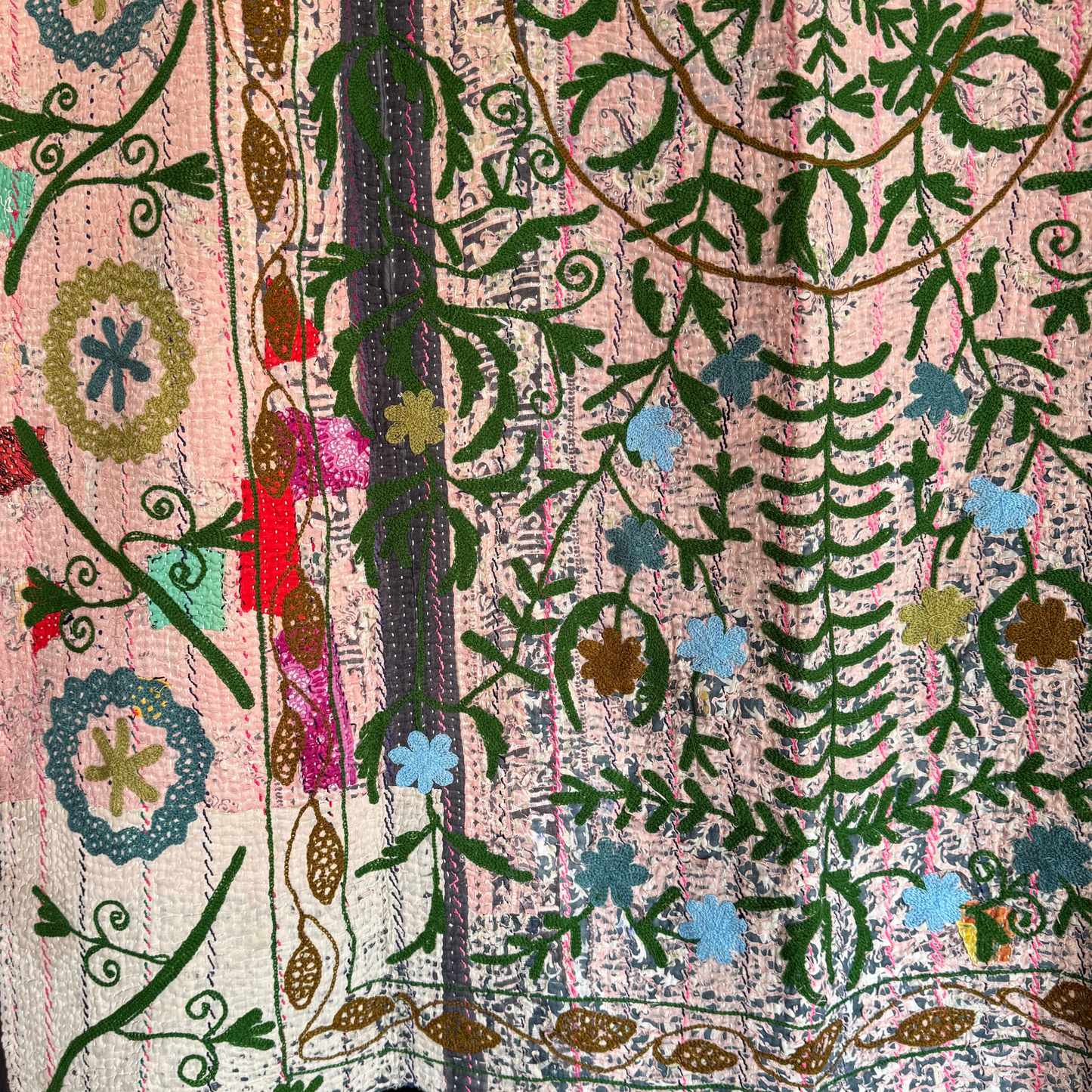 Close-up of kantha embroidery showing scrolling botanical forms on faded pink textile base