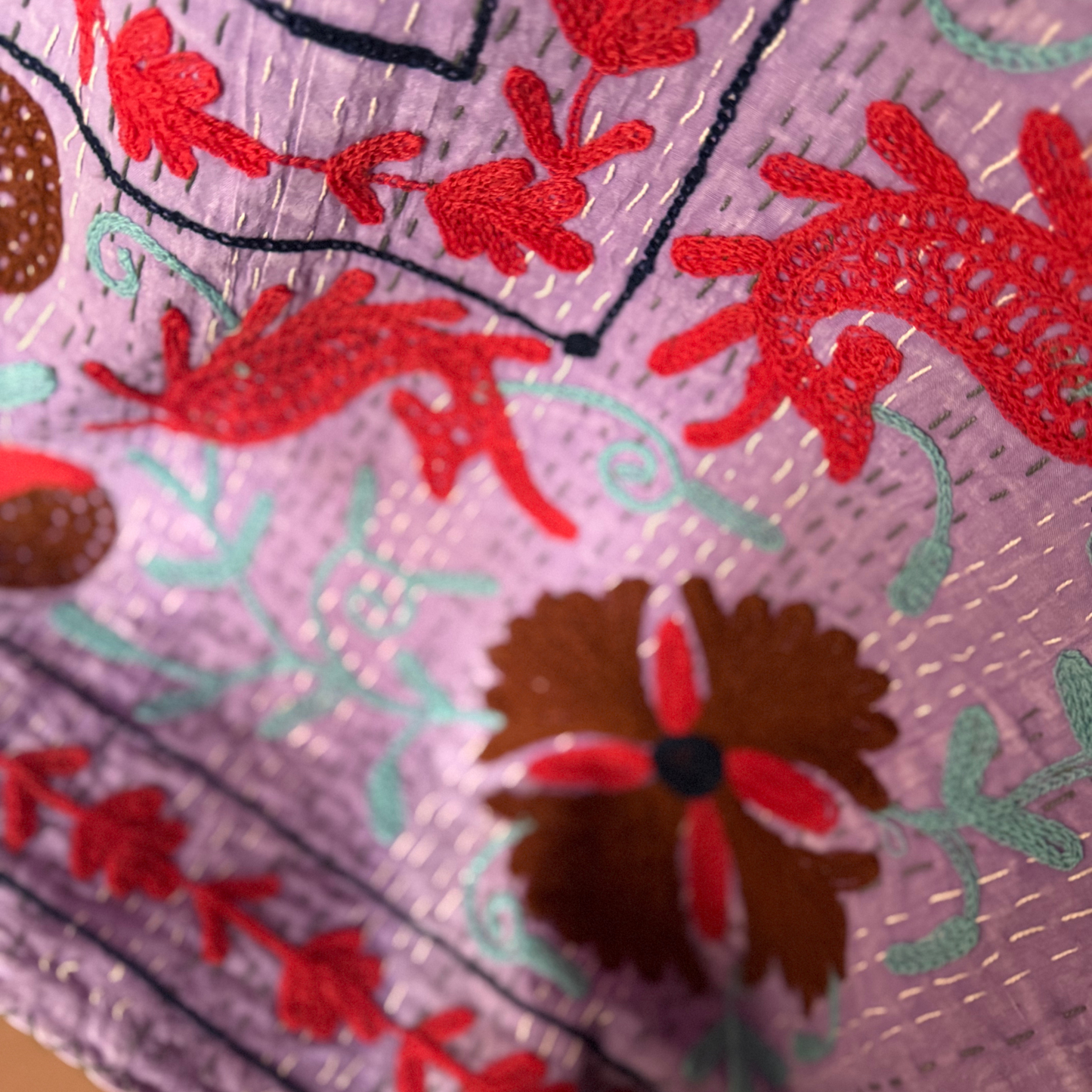 Detailed embroidery showing red animal figures and delicate leaf stitching on cotton