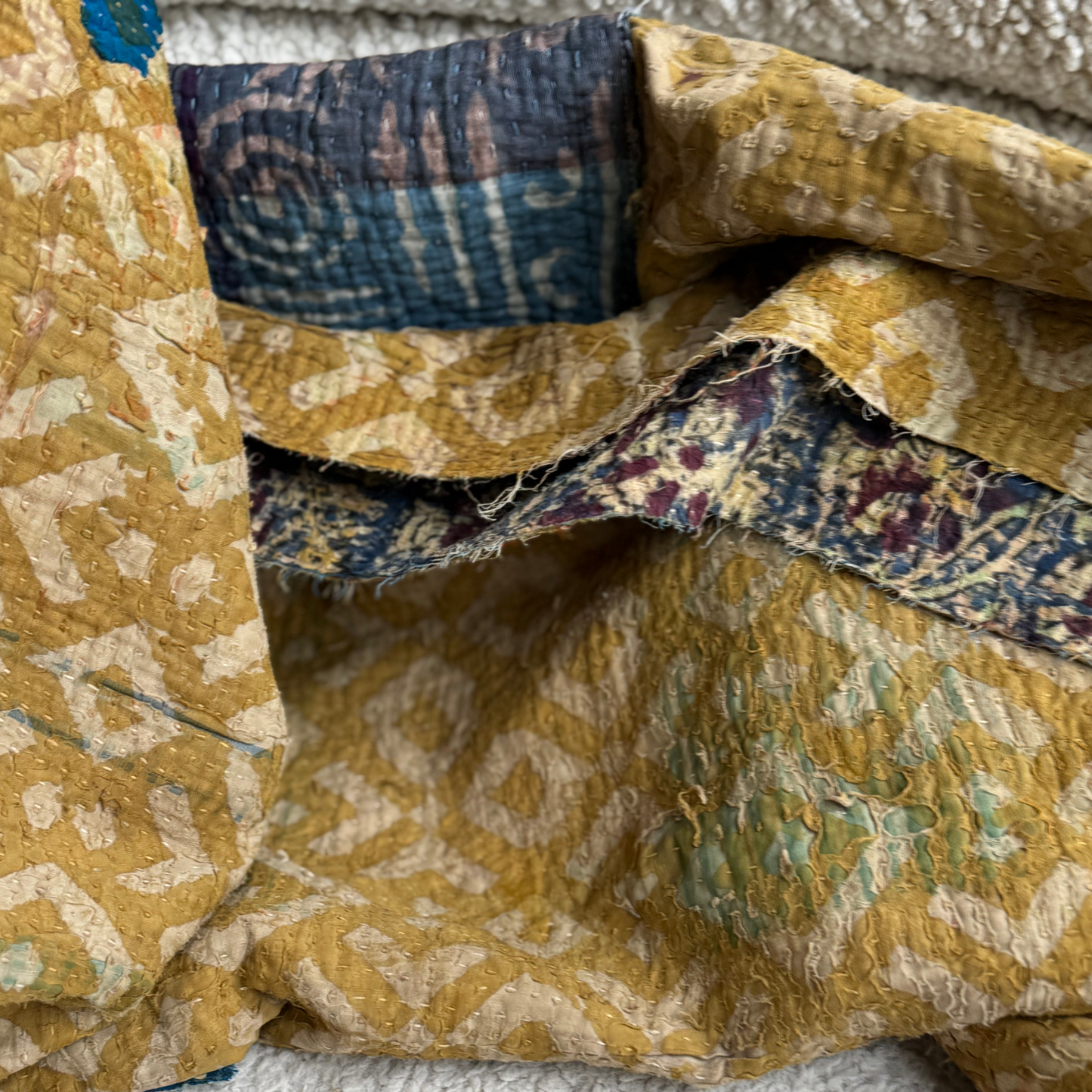 Folded edge of kantha showing signs of wear, layered cotton texture and quilting details