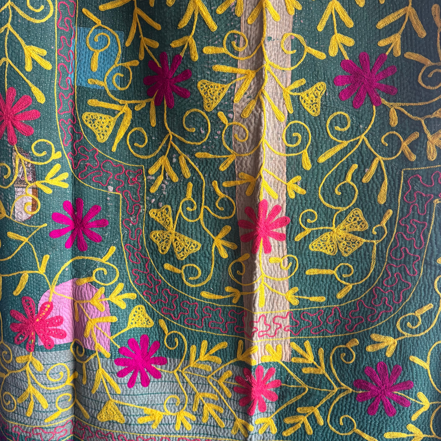 Close-up of yellow vine embroidery and fuchsia flower on grass-green cotton