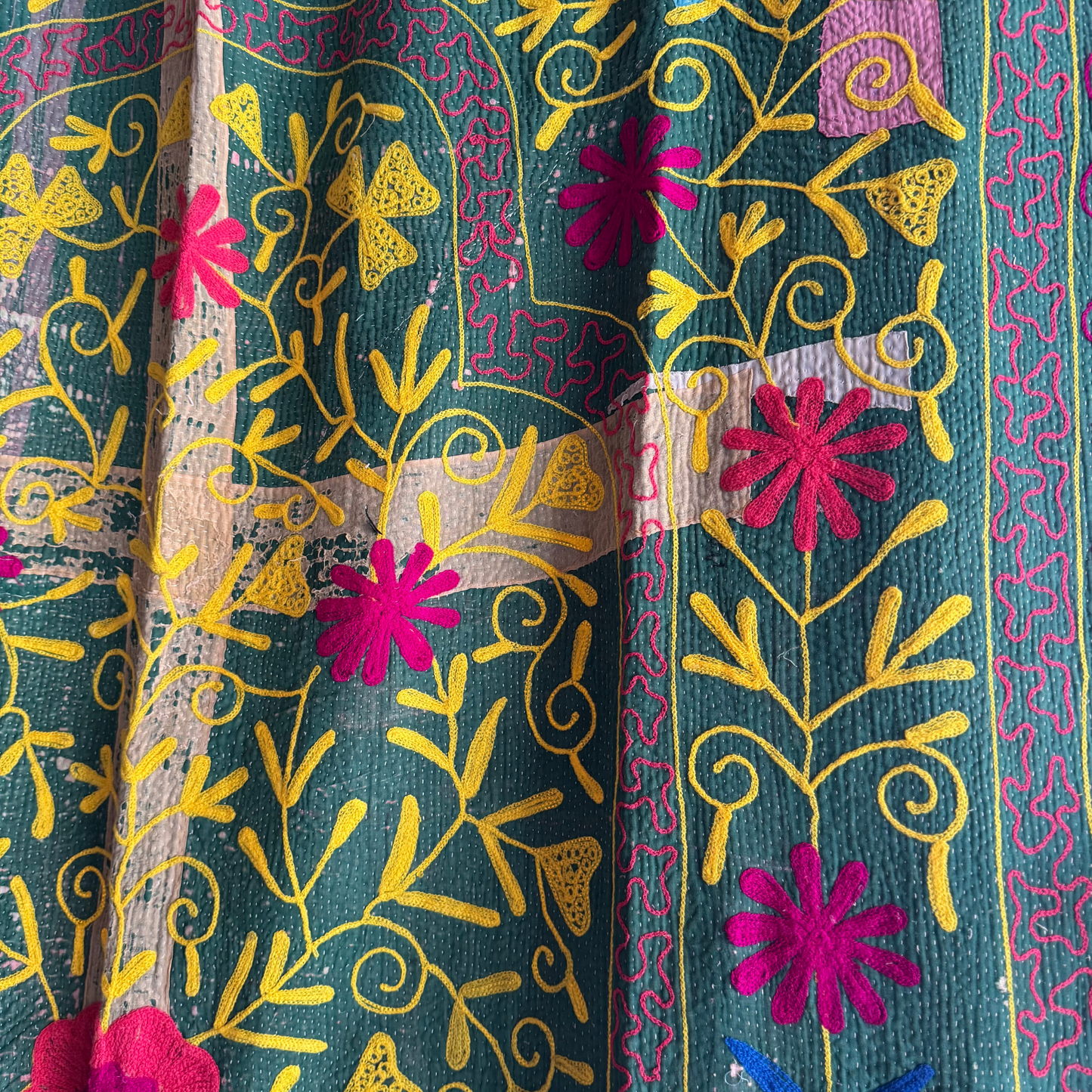 Close-up of yellow vine embroidery and fuchsia flower on grass-green cotton
