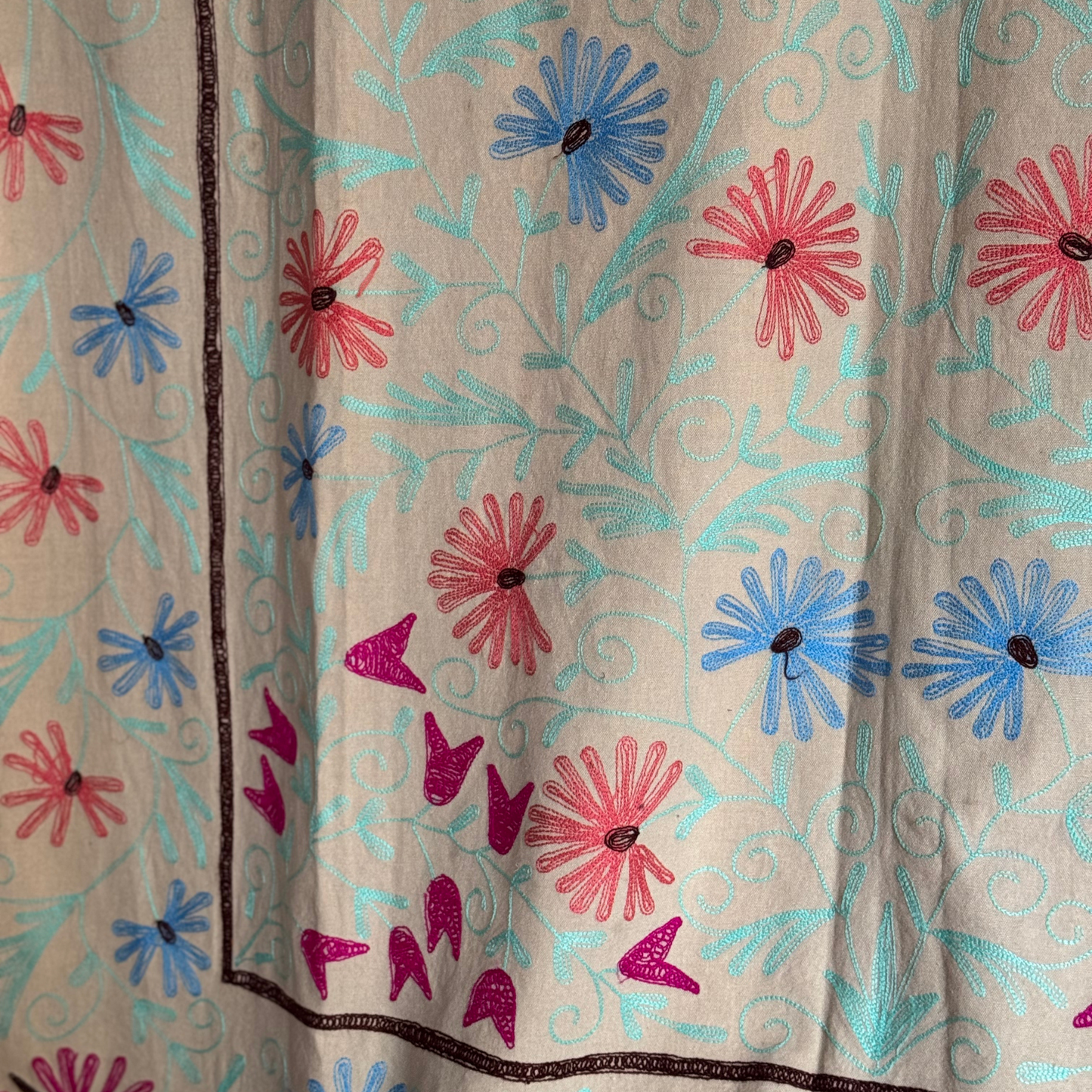 Zoomed embroidery detail with bright pink, aqua, and cobalt blue floral patterns