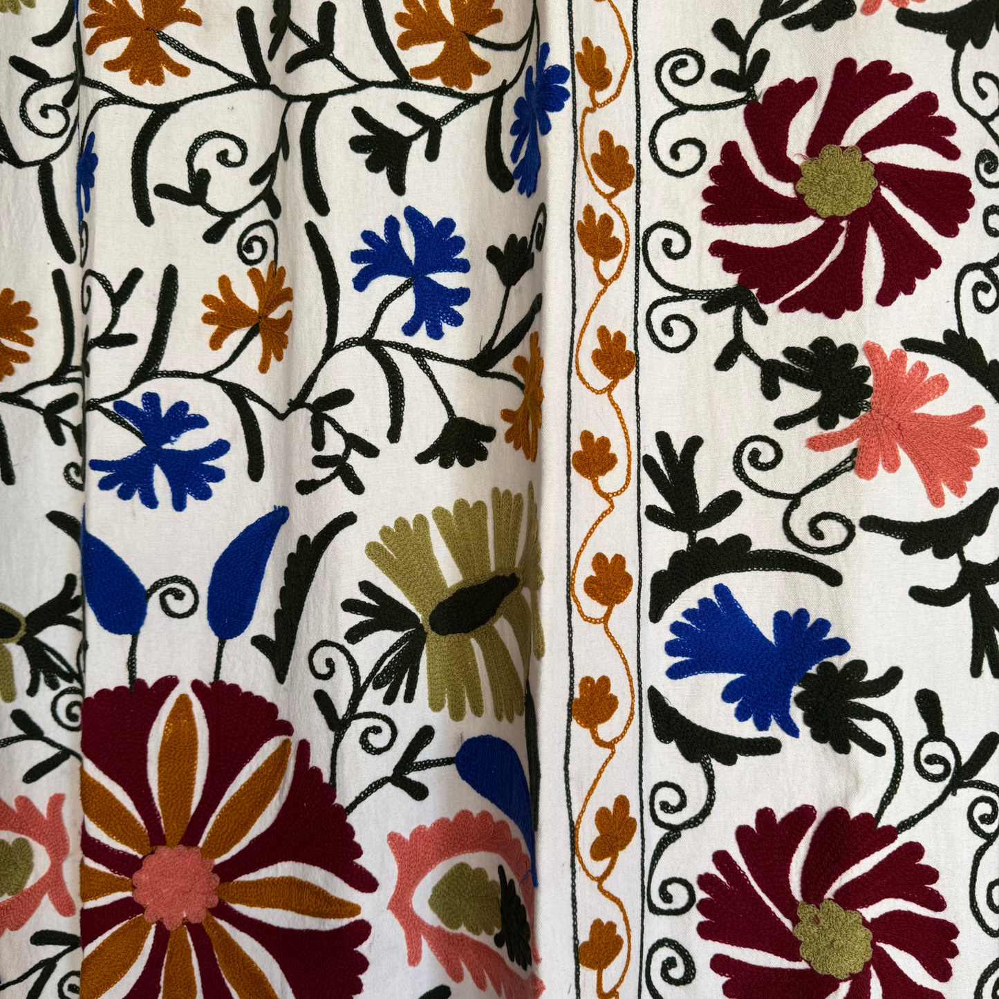 Suzani textile folded over sofa edge showing edge border and colorful embroidery