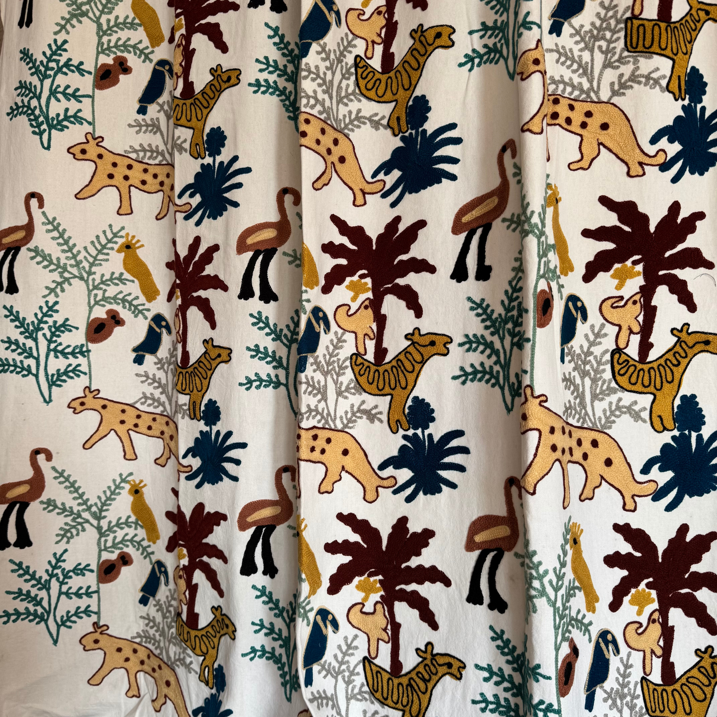 Close-up of mustard-yellow leopard and rust-brown palm tree embroidery on white ground