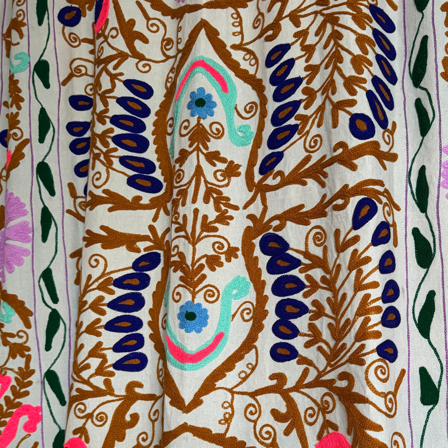 Intricate floral and scroll embroidery in blue, aqua, coral and ochre tones on hand-stitched Suzani