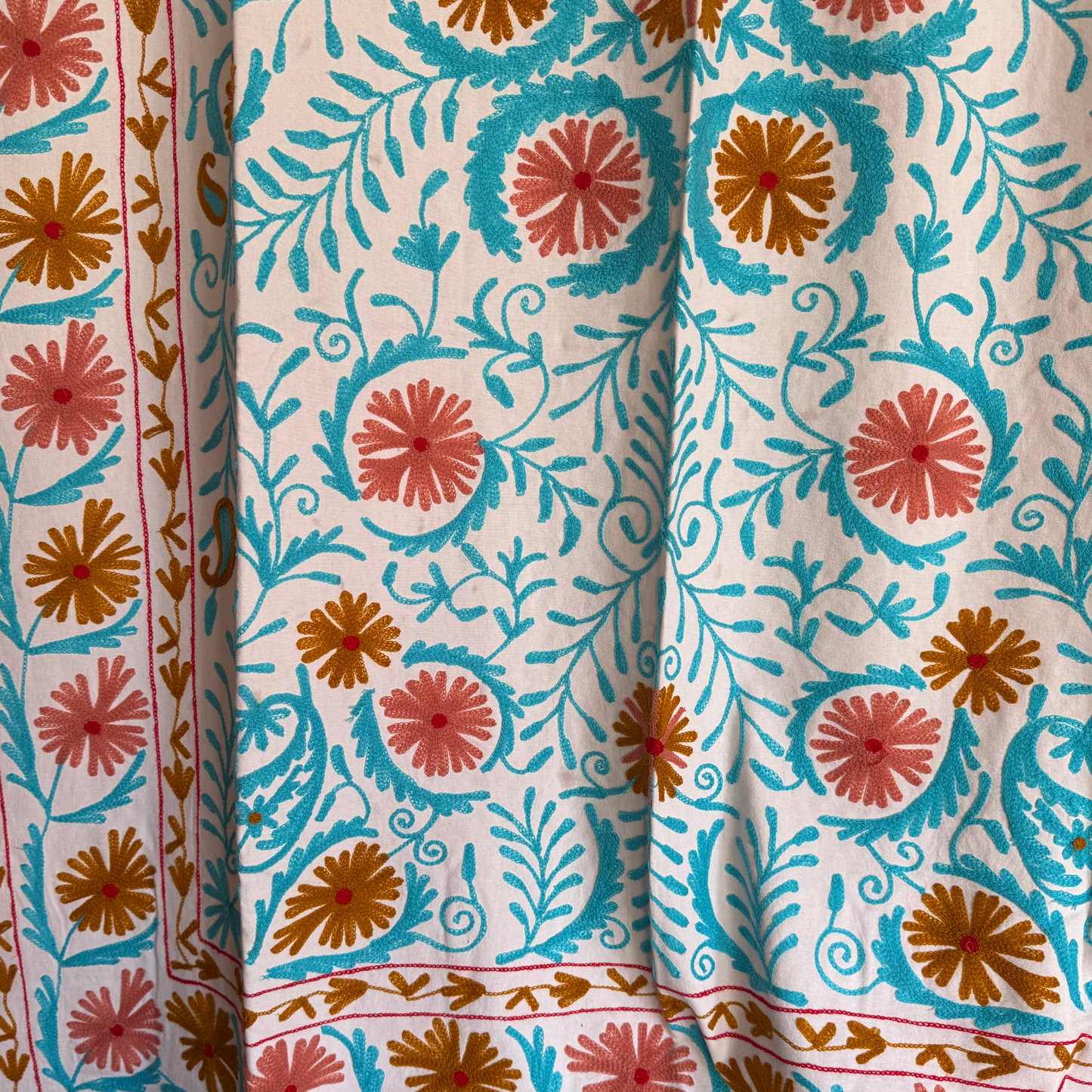Detail shot showing rose and red floral medallions with gold-ochre centers and chain-stitch texture