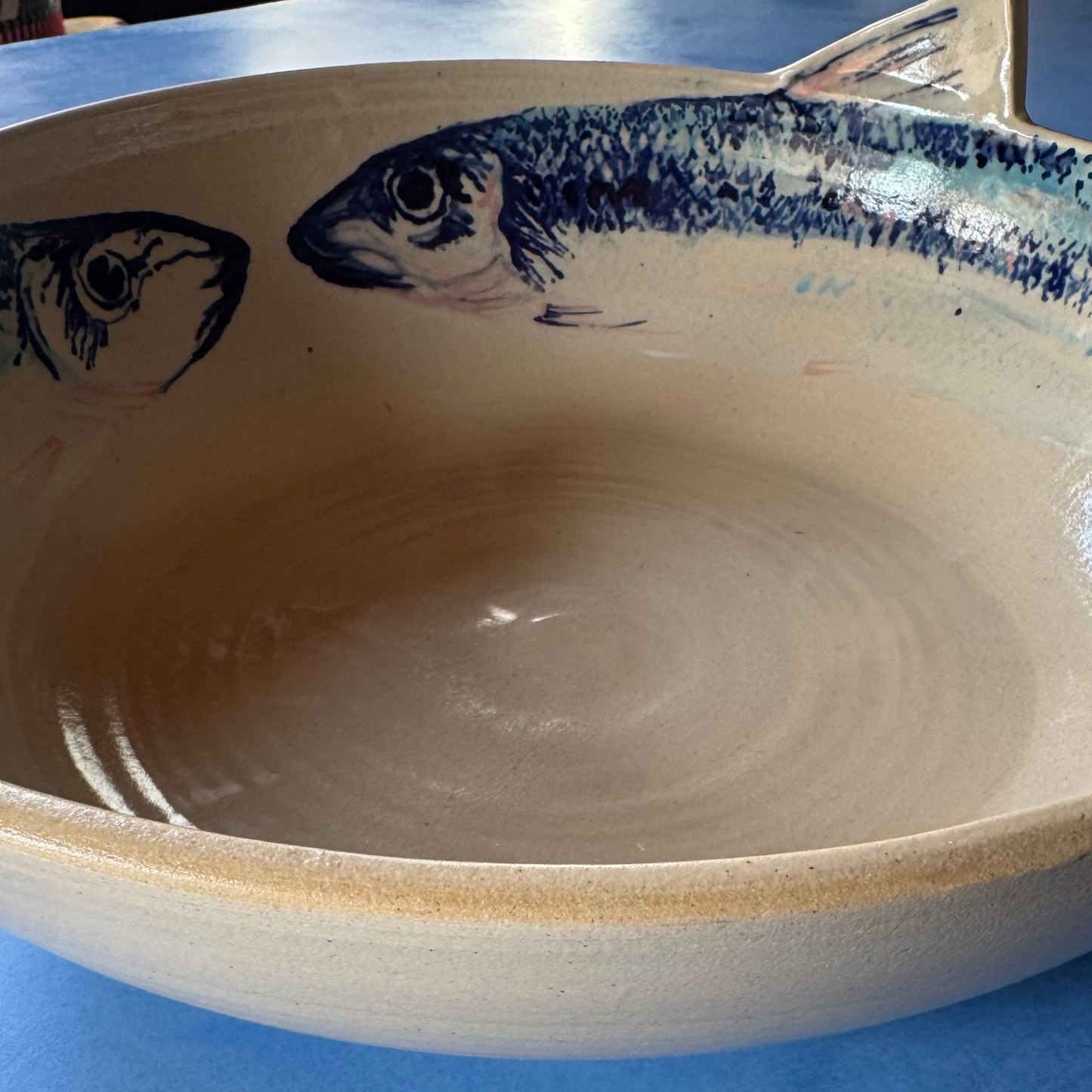 Close-up van het handgeschilderde dorade-visontwerp met blauw en roze accenten op de crèmekleurige keramische kom.