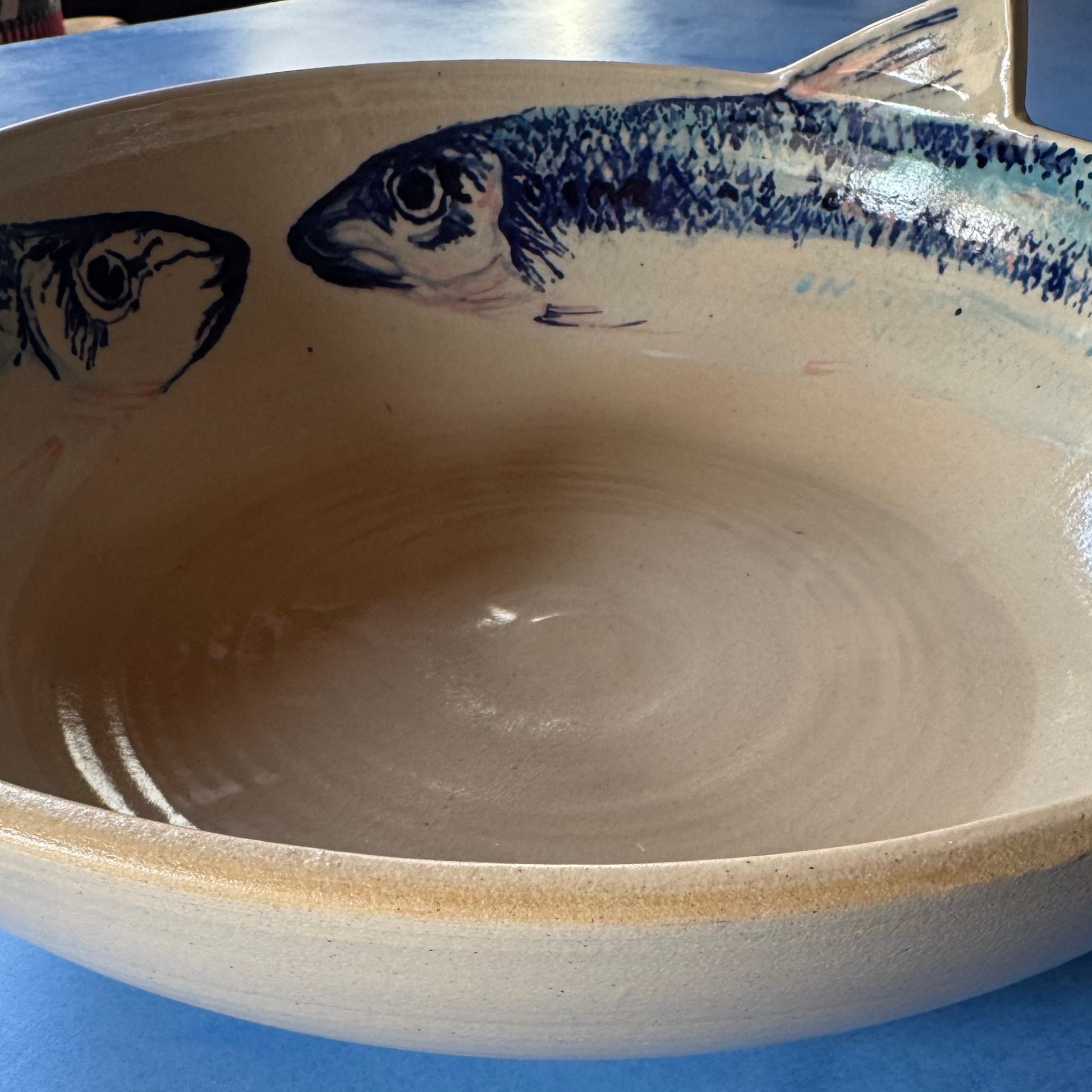 Close-up van het handgeschilderde dorade-visontwerp met blauw en roze accenten op de crèmekleurige keramische kom.