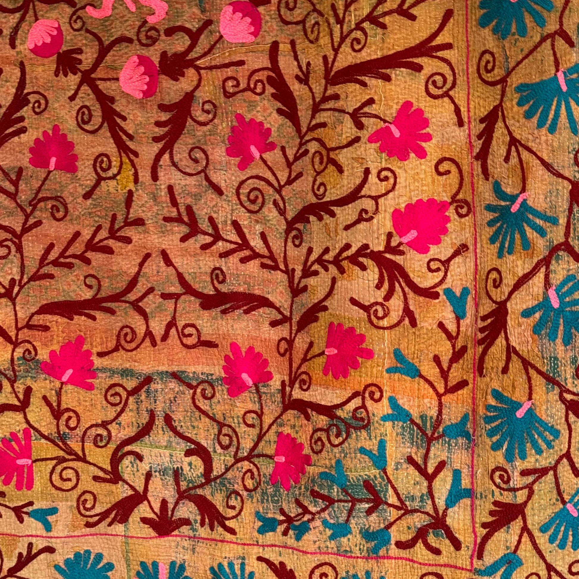 Zoomed embroidery detail of maroon vines and fuchsia flowers on a rich, multi-tonal cotton background