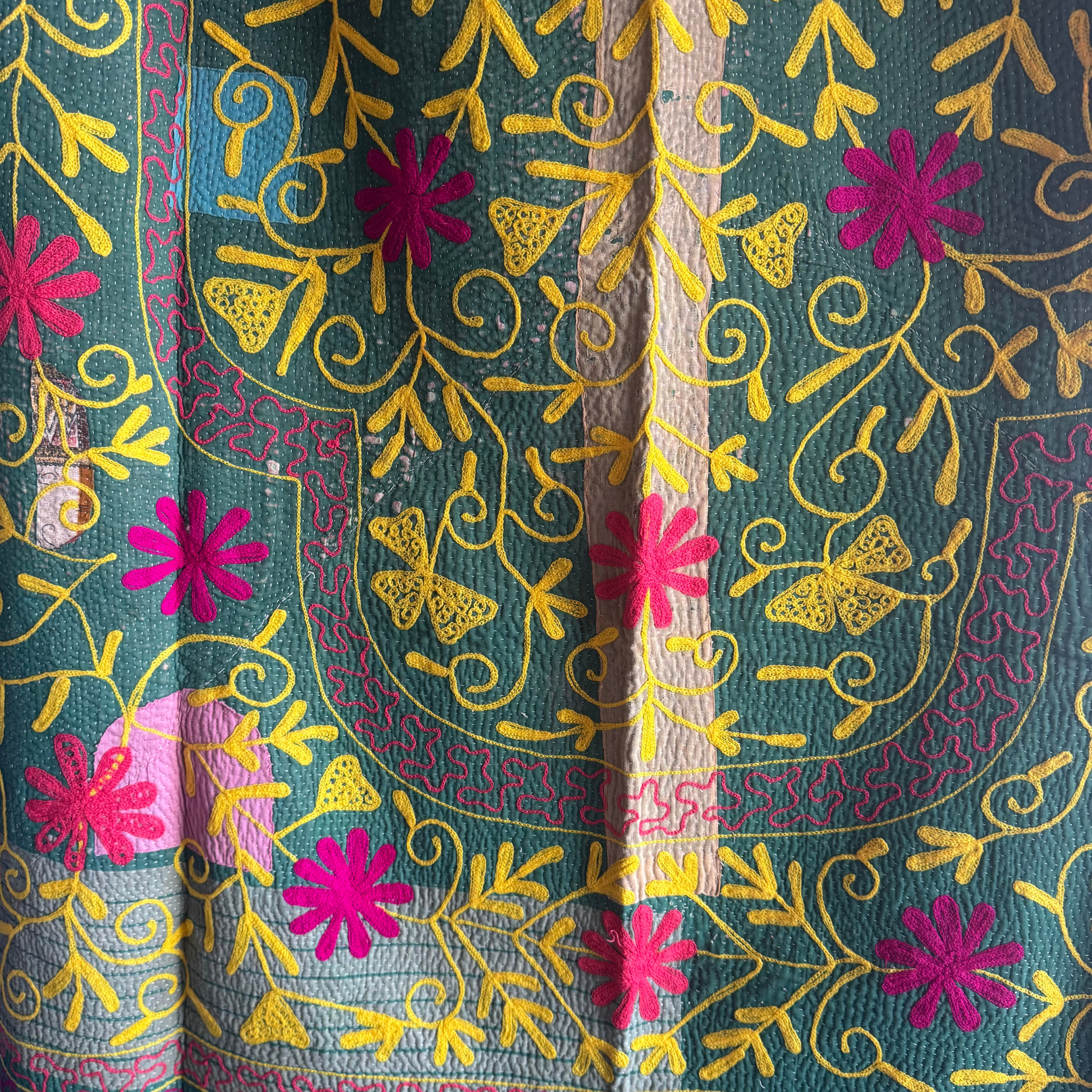 Close-up of yellow vine embroidery and fuchsia flower on grass-green cotton