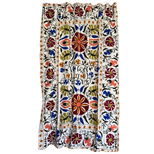 Full view of white cotton Suzani textile with burgundy, cobalt blue, pink and green floral embroidery  