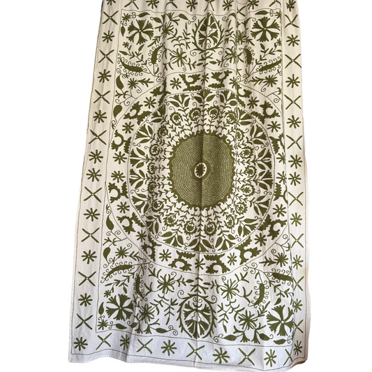 Front view of suzani textile on white cotton ground with central olive-green mandala and vine embroidery