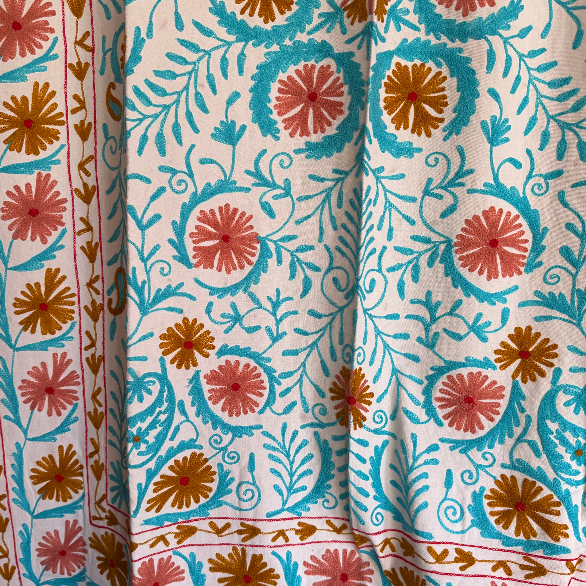 Detail shot showing rose and red floral medallions with gold-ochre centers and chain-stitch texture